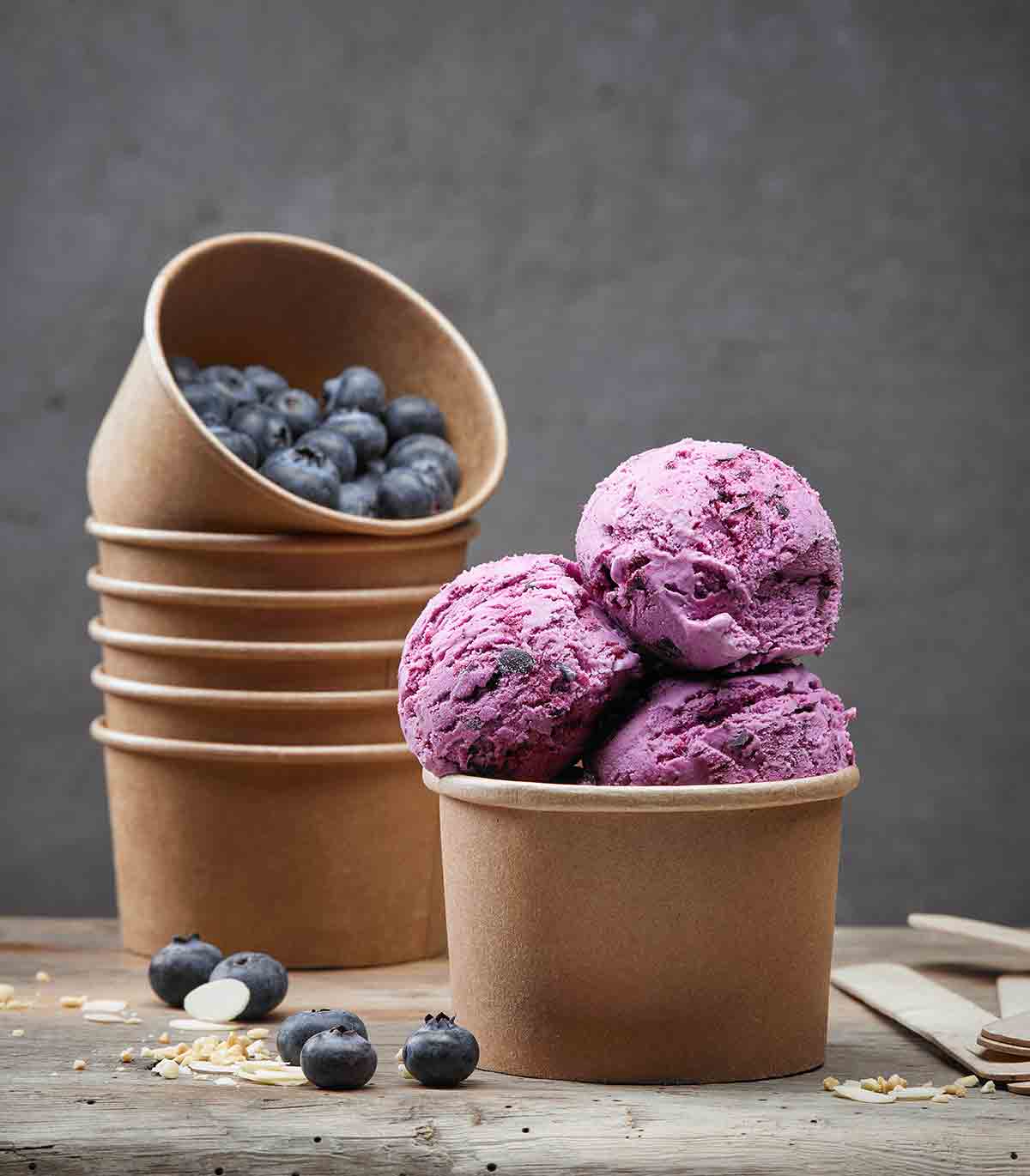 A brown container with three scoops of blueberry ice cream, in the back a stack of containers