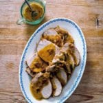 Braised pork loin with rosemary topped with a mustard-garlic sauce on a white plate on wood