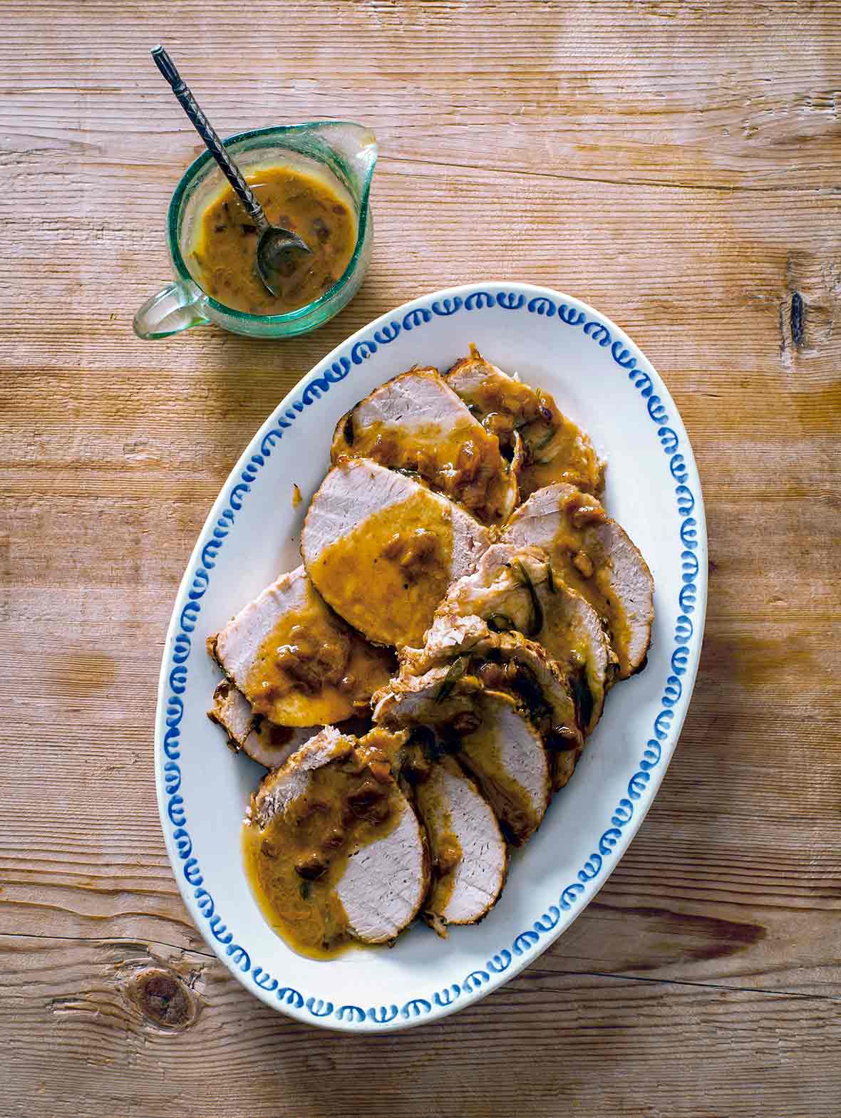 Braised pork loin with rosemary topped with a mustard-garlic sauce on a white plate on wood