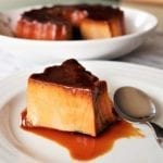 A piece of Portuguese tea flan on a white plate, drizzled with caramel sauce with the remaining flan in a bowl in the background.