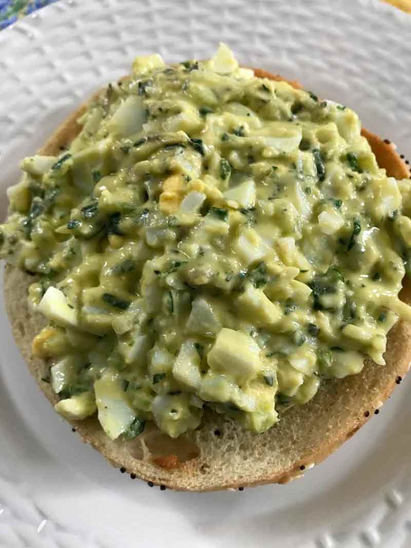 Egg salad made with yogurt and chives placed on an open-face bagel sandwich