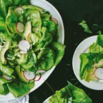 Spring salad with shallot vinaigrette with sliced radishes, avocados, and chives on three plates