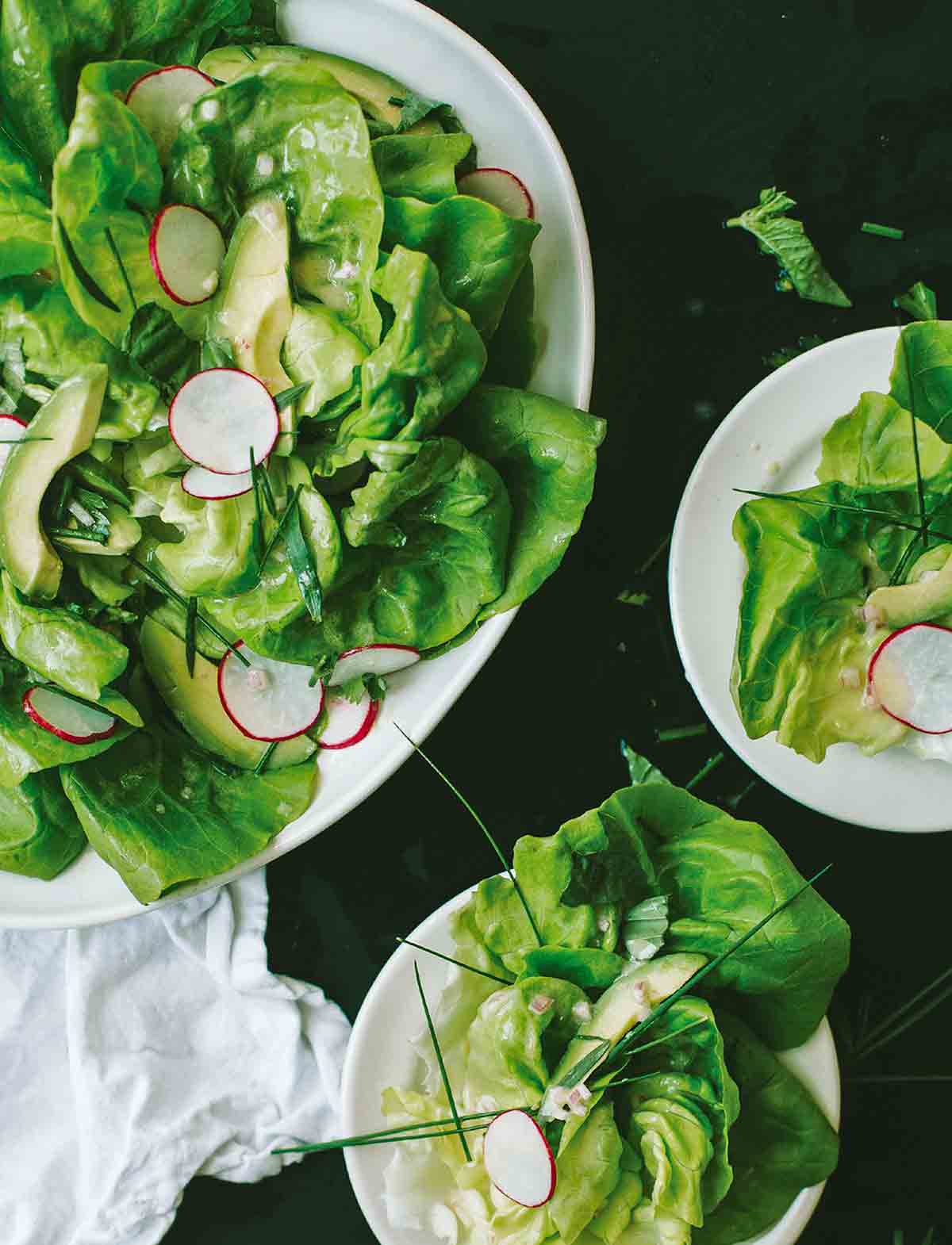 Spring salad with shallot vinaigrette with sliced radishes, avocados, and chives on three plates.