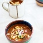 A pottery bowl filled with tortilla soup, garnished with radish, cotija cheese, tortilla strips, and avocado.