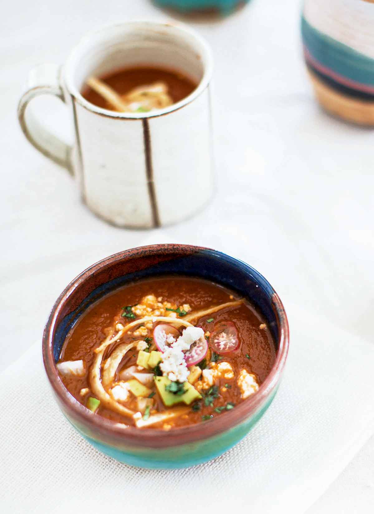 A pottery bowl filled with tortilla soup, garnished with radish, cotija cheese, tortilla strips, and avocado.