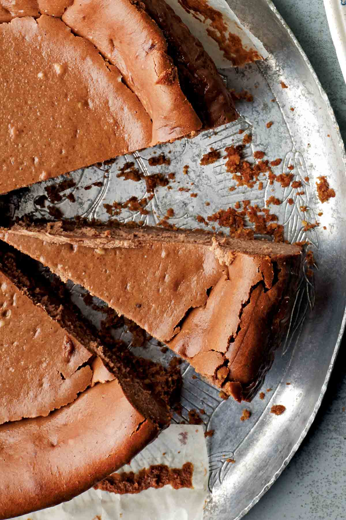 An espresso cheesecake on a silver platter with two slices cut from it.