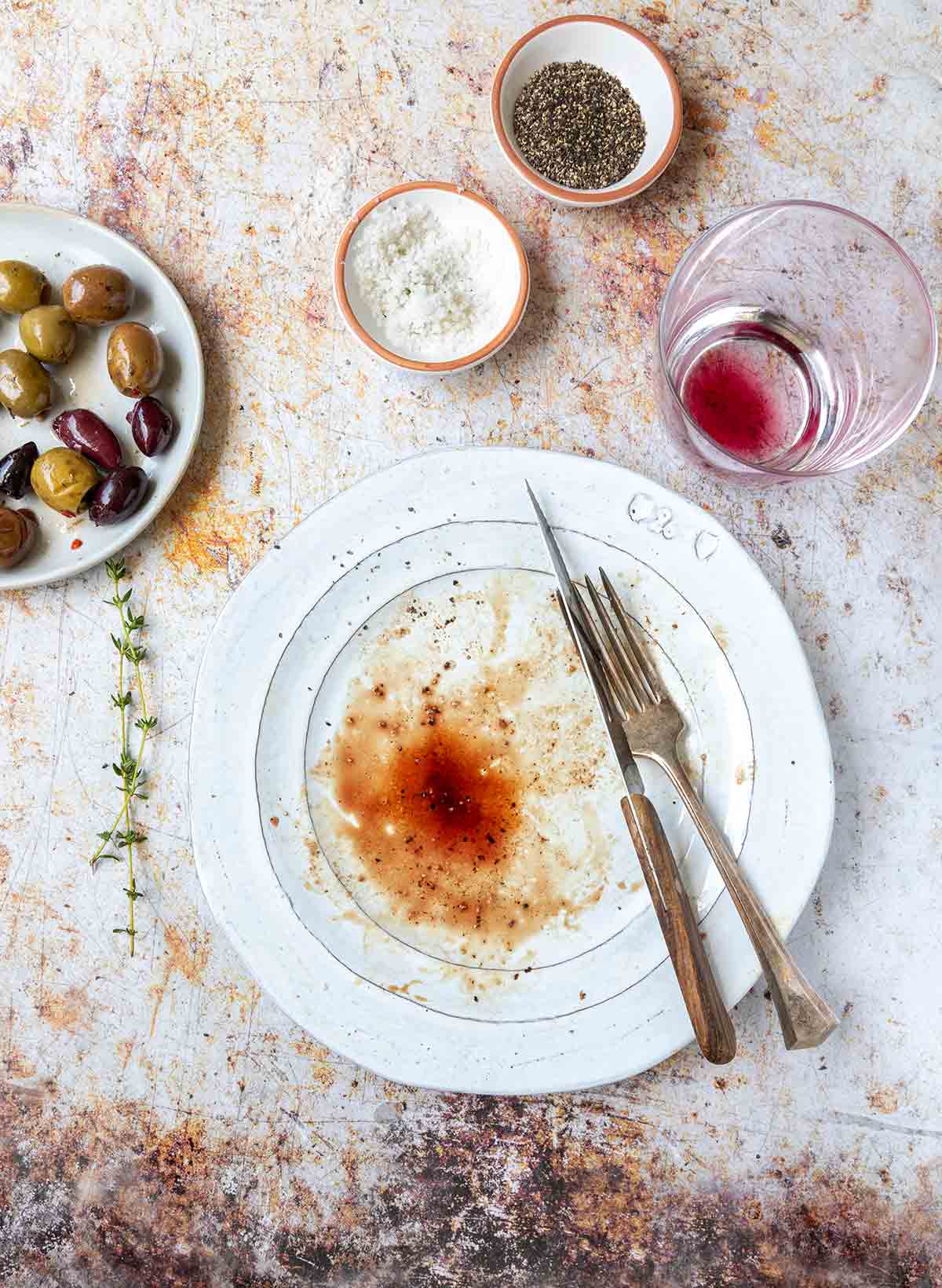 En vit tallrik med biffjuice och blod på, ett glas vin och oliver i närheten