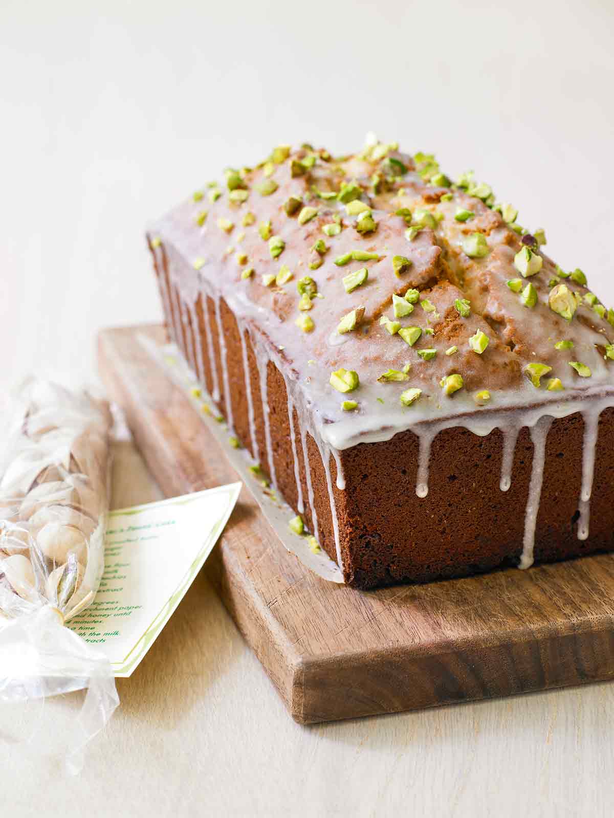 A pistachio lover's pound cake on a wooden cutting board with a mesh bag of pistachios beside it.