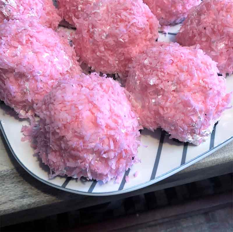 Seven homemade pink sno-balls, like Hostess Sno-balls, covered in meringue and pink coconut on a blue and white tray