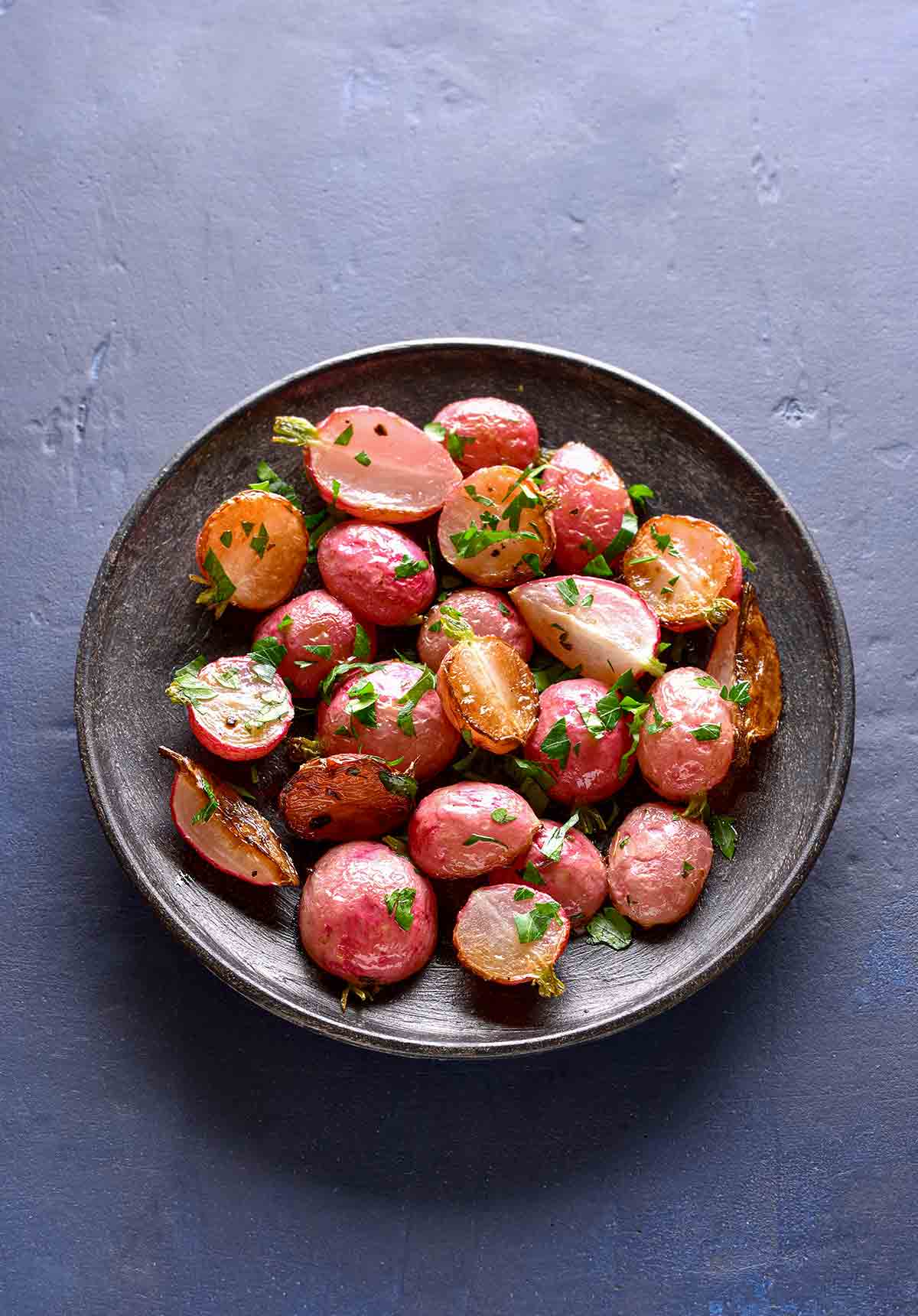 A grey bowl filled with roasted radishes, sprinkled with thyme.