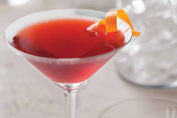 A martini glass filled with a red negroni drink with a twist or orange peel.