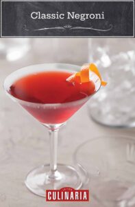 A martini glass filled with a red negroni drink with a twist or orange peel.