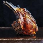 A deeply browned grilled rack on lamb sitting on a black surface