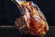 A deeply browned grilled rack on lamb sitting on a black surface.