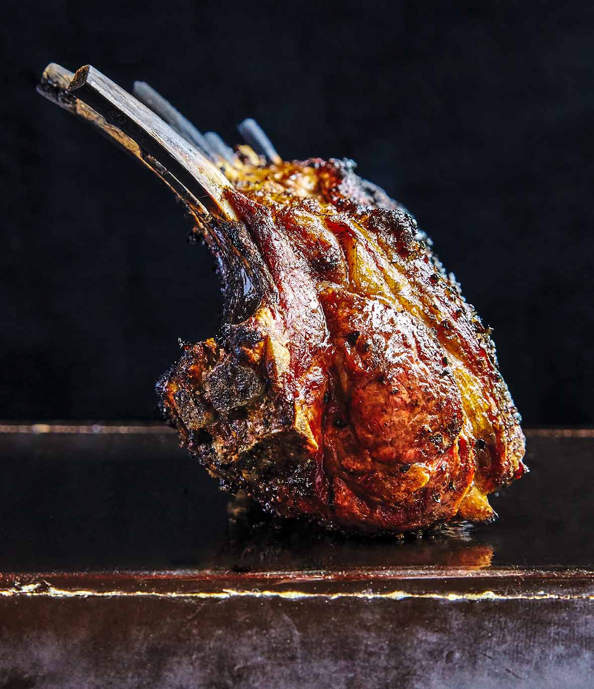 A deeply browned grilled rack on lamb sitting on a black surface.