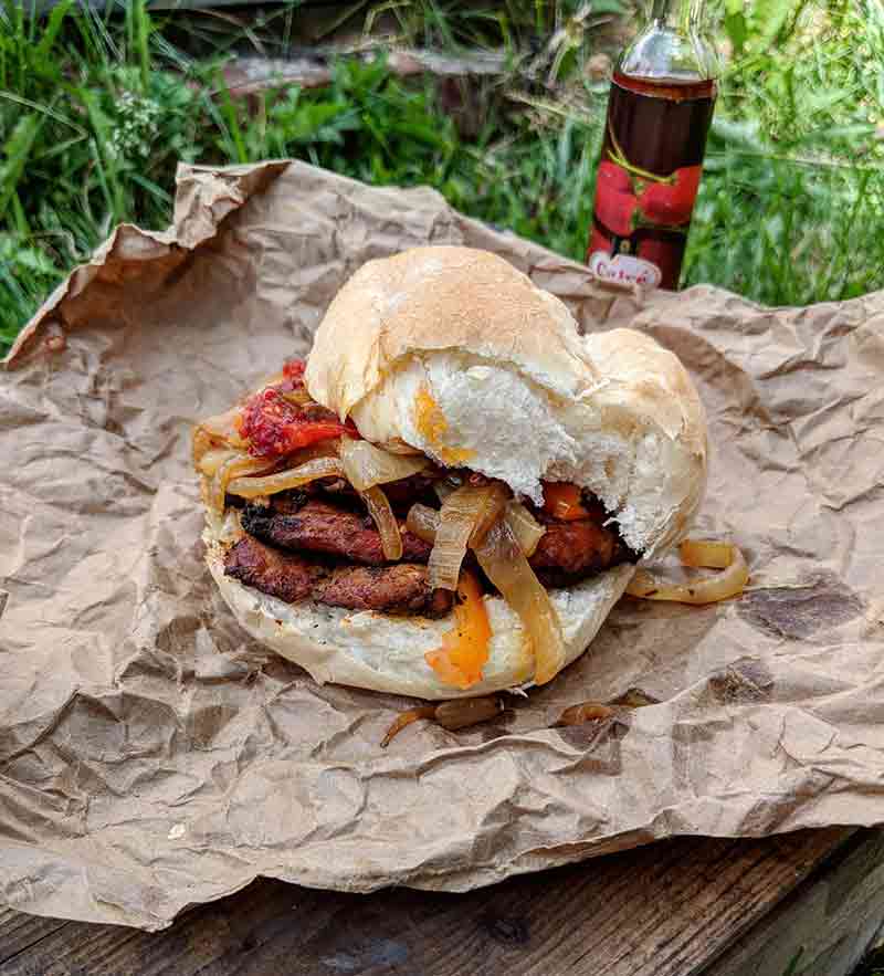 A bifana--Portuguese pork sandwich--with sauteed onions and peppers on a roll, on brown wrapping paper, sitting on grass