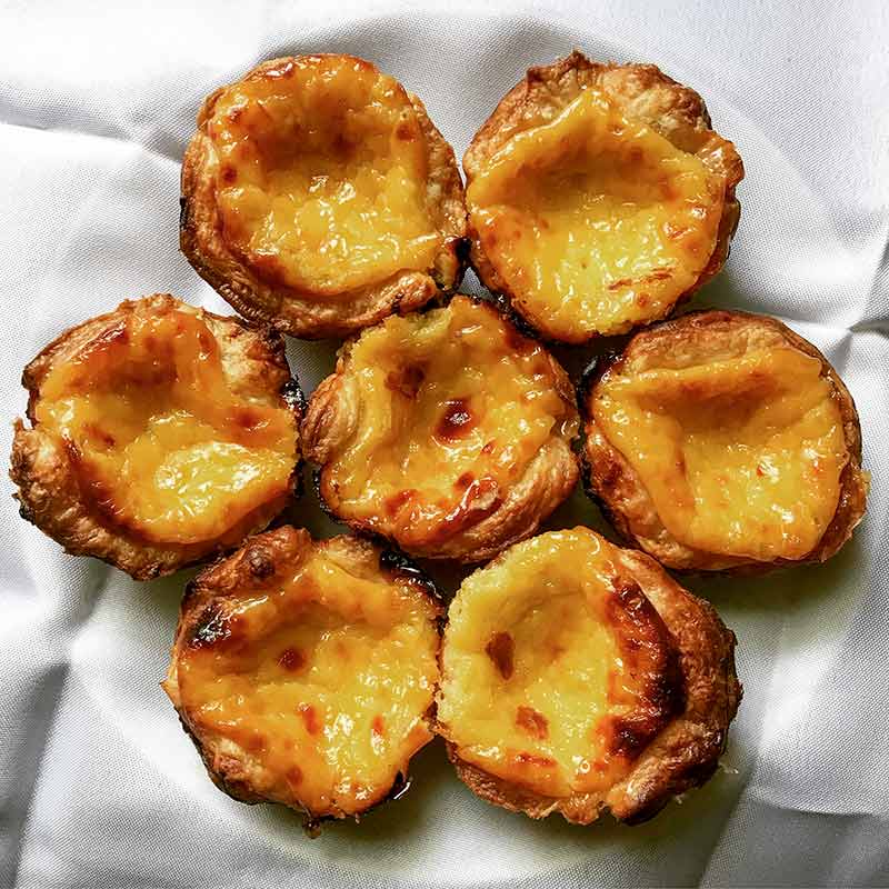 Seven pastéis de nata--Portuguese custard pastries with flakey shells filled with a mottled burnt surface