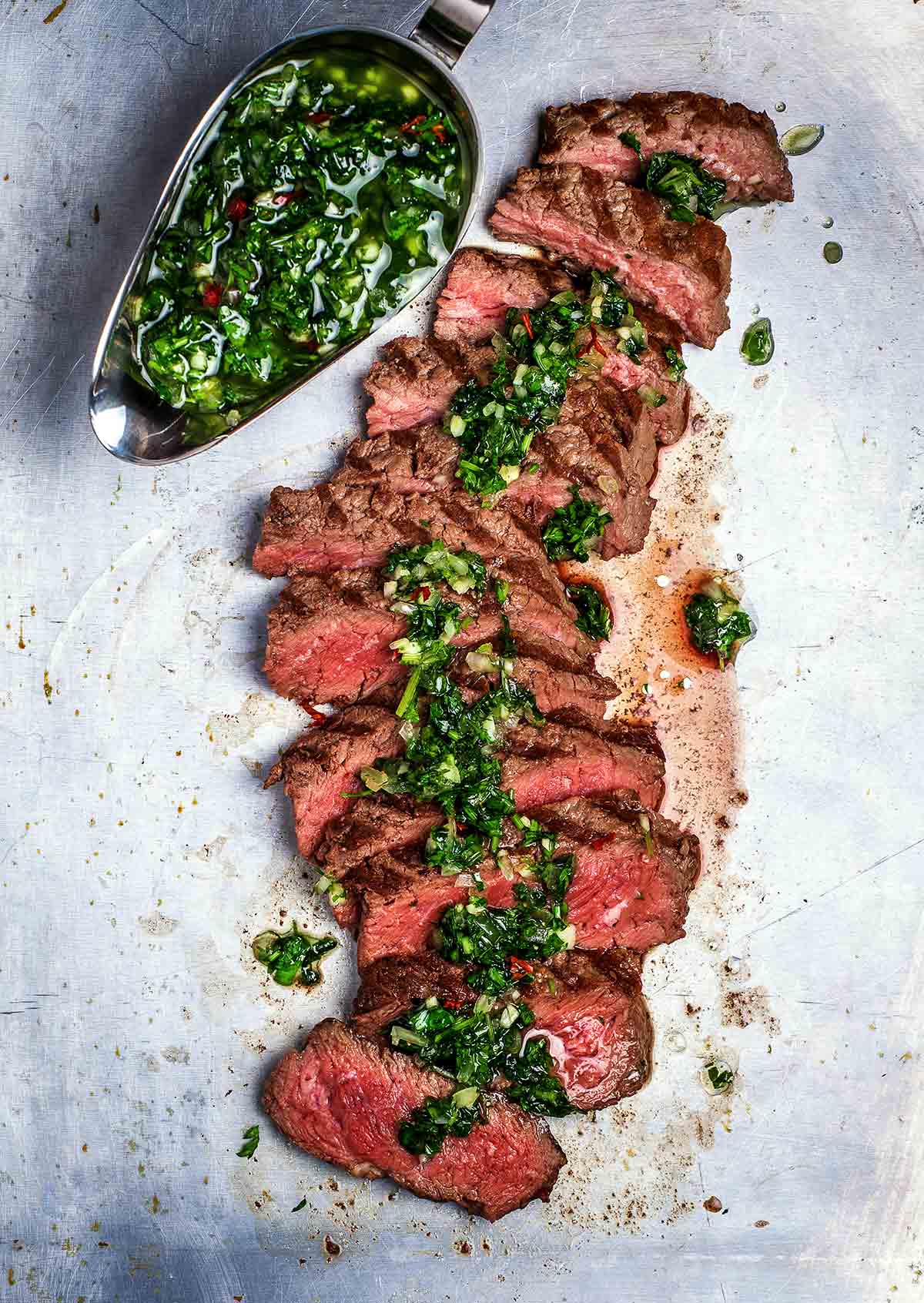 A sliced steak chimichurri with a gravy boat filled with chimichurri on the side.