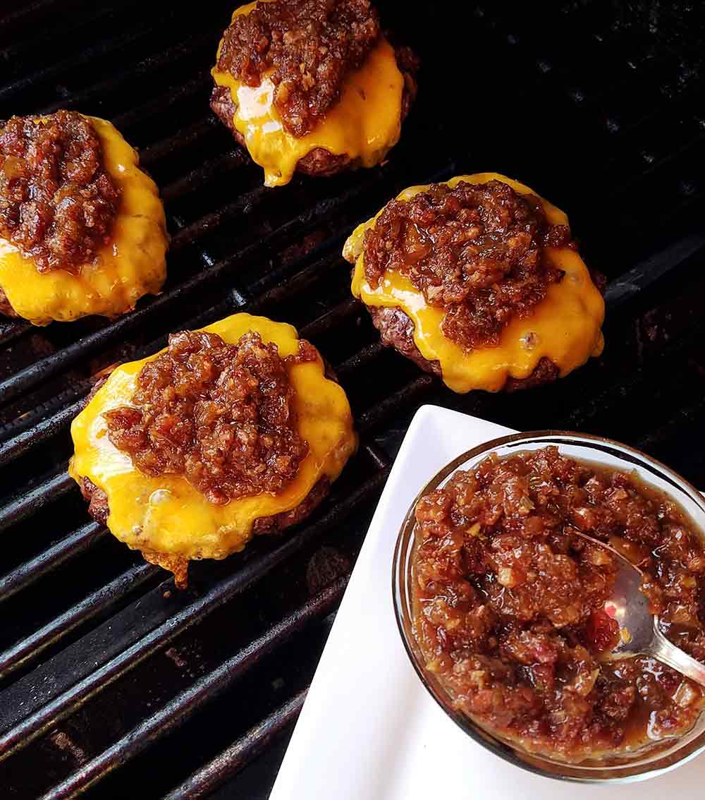 Four cheese burgers on a grill topped with bacon jam