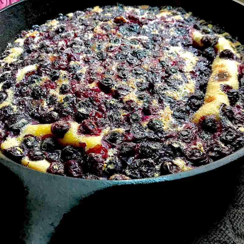 A cast iron skillet filled with blueberry clafouti--golden cake speckled with blueberries