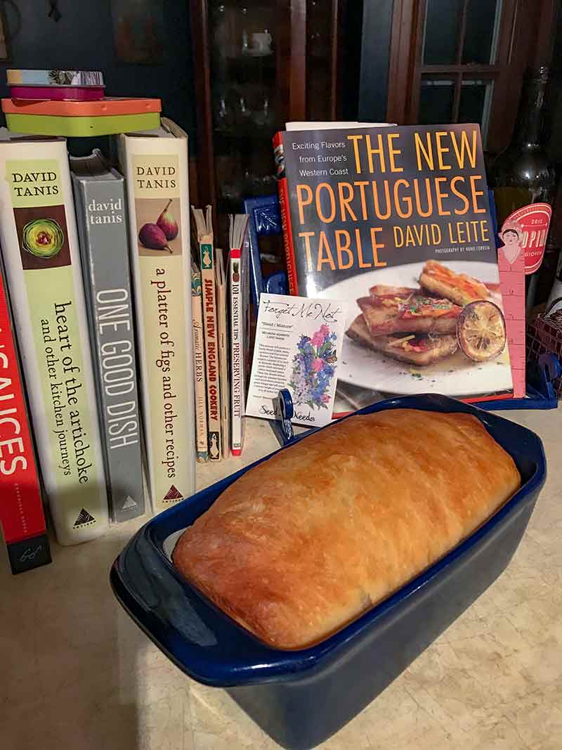 a loaf of homemade sandwich bread in a pan in front of cookbooks