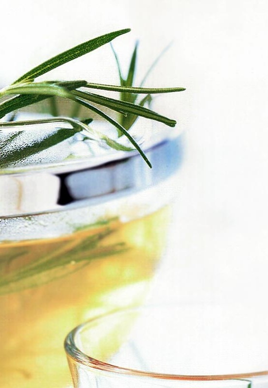 A pot of rosemary infused tea with rosemary sprigs sticking out the top and a glass beside it.