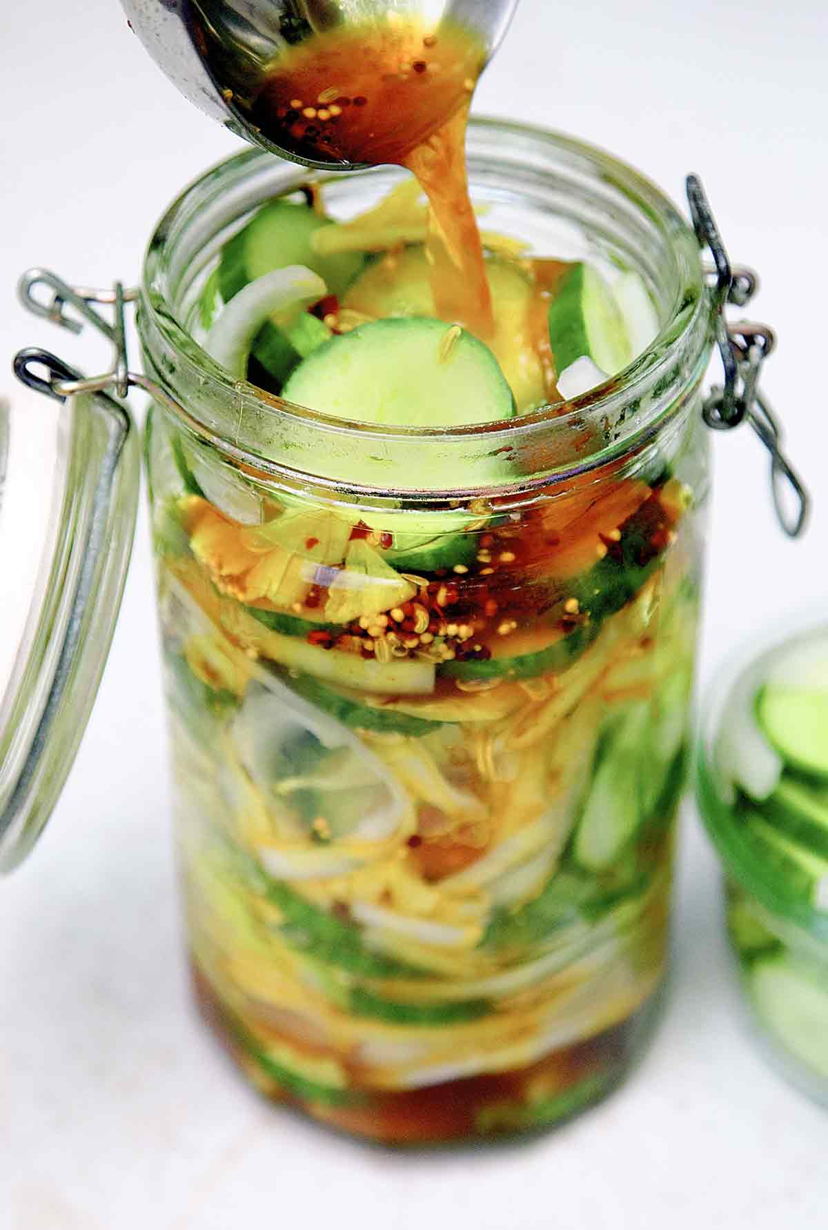 A glass canning jar filled with bread and butter pickles, with pickling liquid being poured over.
