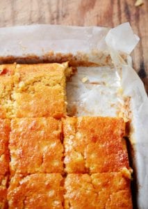 A parchment-lined square pan of buttermilk cornbread cut into squares, with one square missing.
