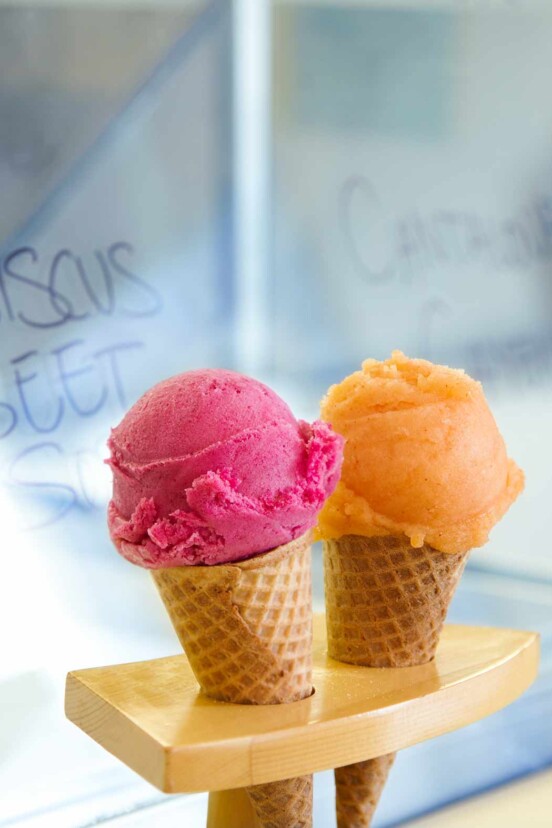 Two sugar cones, one filled with a scoop of cantaloupe sorbet, the other with a scoop of hibiscus sorbet.