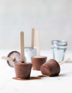 Chocolate fudge pops with popsicle sticks melting on a white surface.