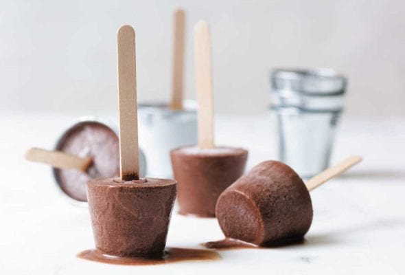 Chocolate fudge pops with popsicle sticks melting on a white surface.