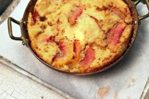 A pan with two handles filled with a Southern peach cobbler on a baking sheet