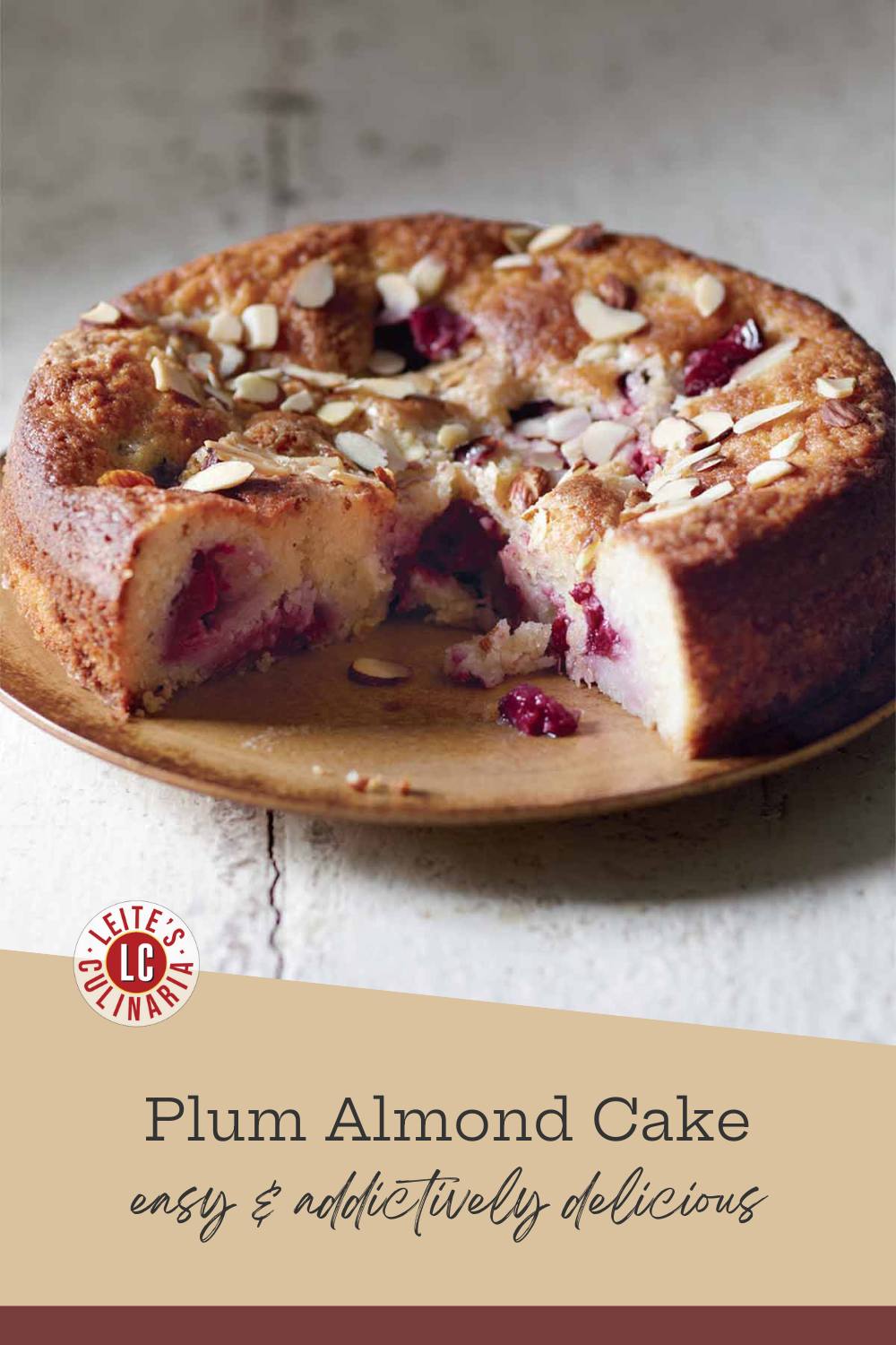 A slice cut from a plum almond cake on a rustic wooden plate, revealing the jammy plum interior and golden-brown crust.