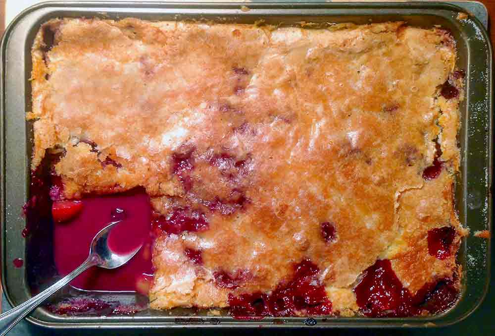 A rectangular baking dish with a peach cobbler, with one corner scooped out