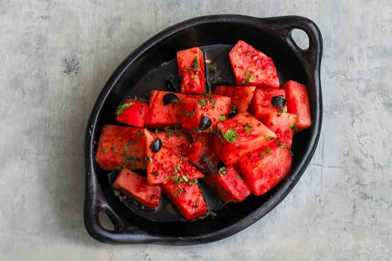 A black oval dish filled with watermelon salad with Aleppo pepper and black olives.