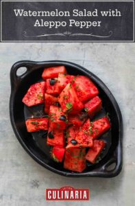 A black oval dish filled with watermelon salad with Aleppo pepper and black olives.