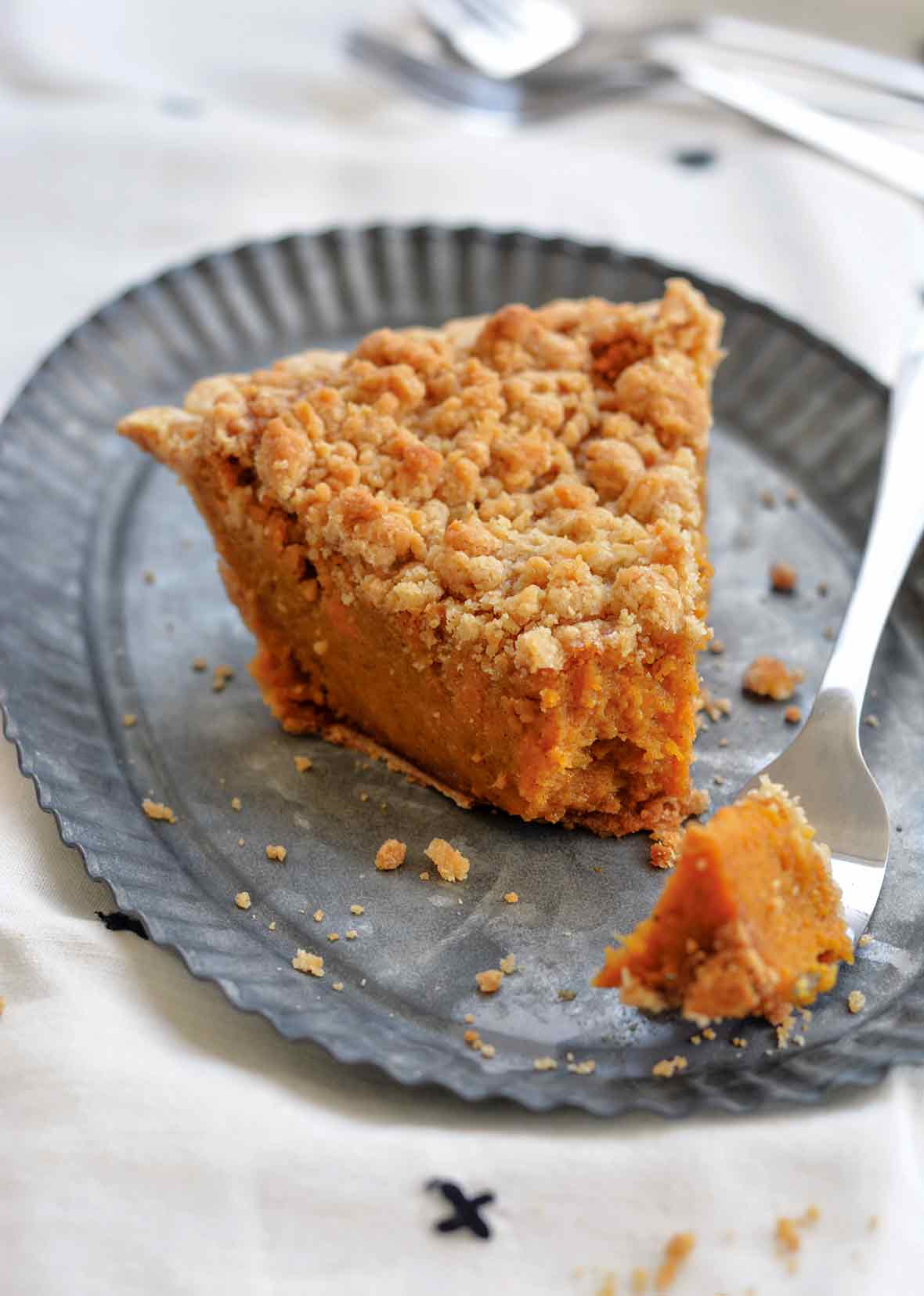 A wedge of bourbon sweet potato pie topped with a crumbly brown sugar streusel omn a metal plate