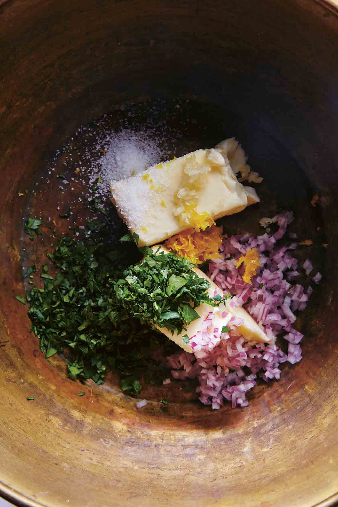 A clay bowl filled with butter, parsley, red onion, lemon zest, orange zest, and salt