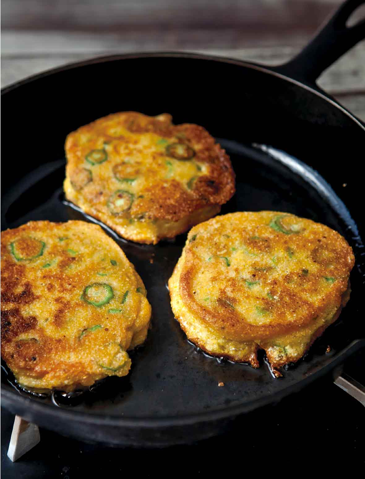 Three okra cornmeal cakes--with rings of green okra in it--in a black cast iron skillet