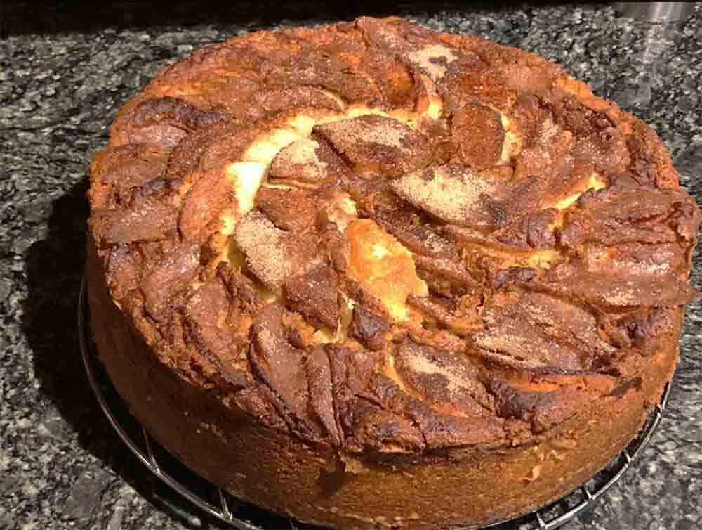 A whole super moist apple cake, whose top is covered with overlapping apple slices topped in brown sugar