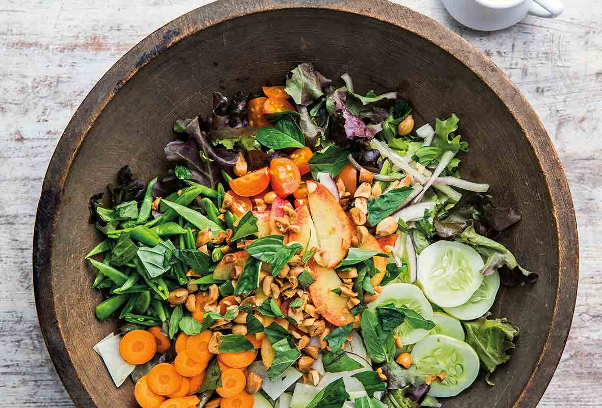 Wooden bowl with vegan gado gado salad--carrots, cucumber, tomatoes, lettuce, peaches, green beans