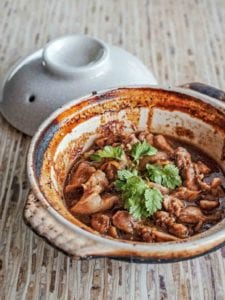 A clay pot of chunks of Vietnamese caramel chicken in ginger sauce, topped with cilantro