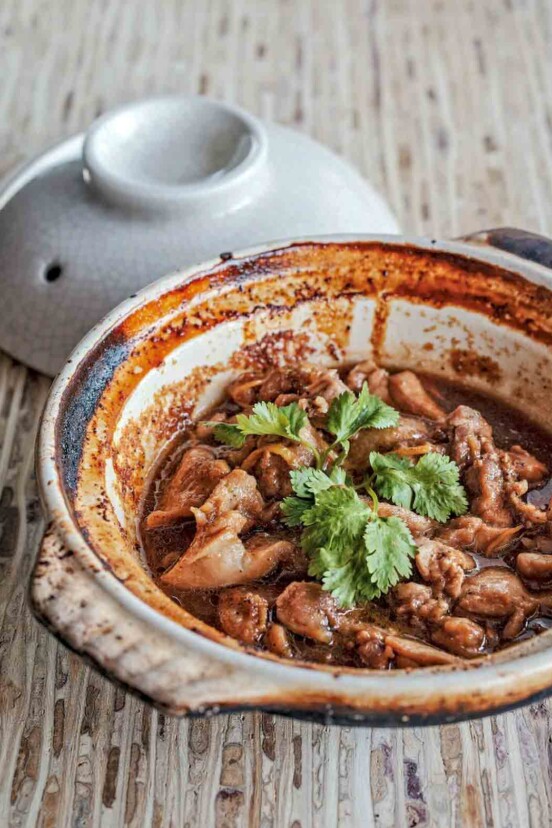 A clay pot of chunks of Vietnamese caramel chicken in ginger sauce, topped with cilantro