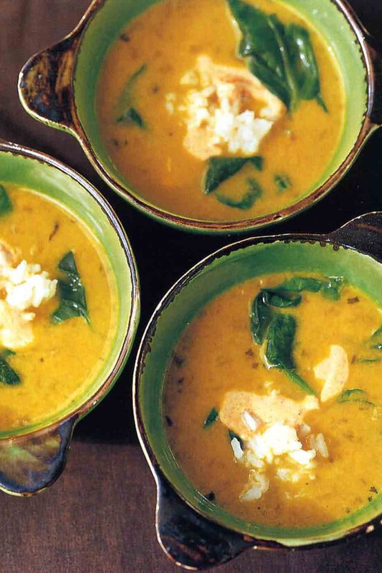 Three bowls of yellow pea and coconut milk soup with pieces of spinach and a dollop of yogurt in each bowl.