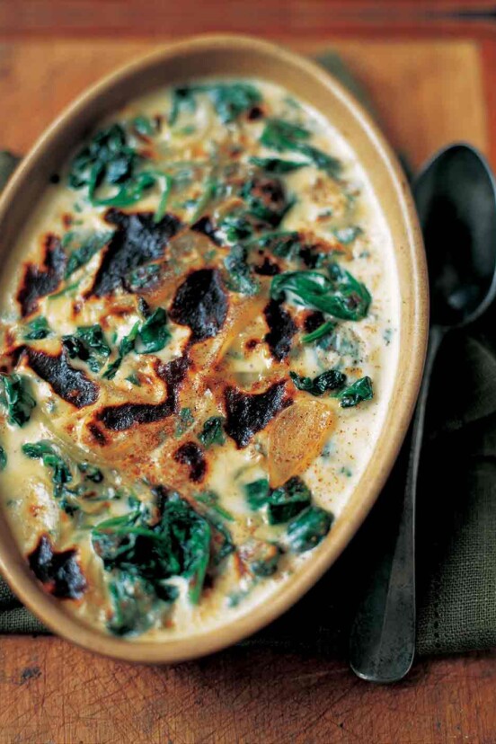 A ceramic oval dish of baked spinach mornay with cream sauce, sliced onion, and browned top.