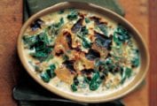 A ceramic oval dish of baked spinach mornay with cream sauce, sliced onion, and browned top