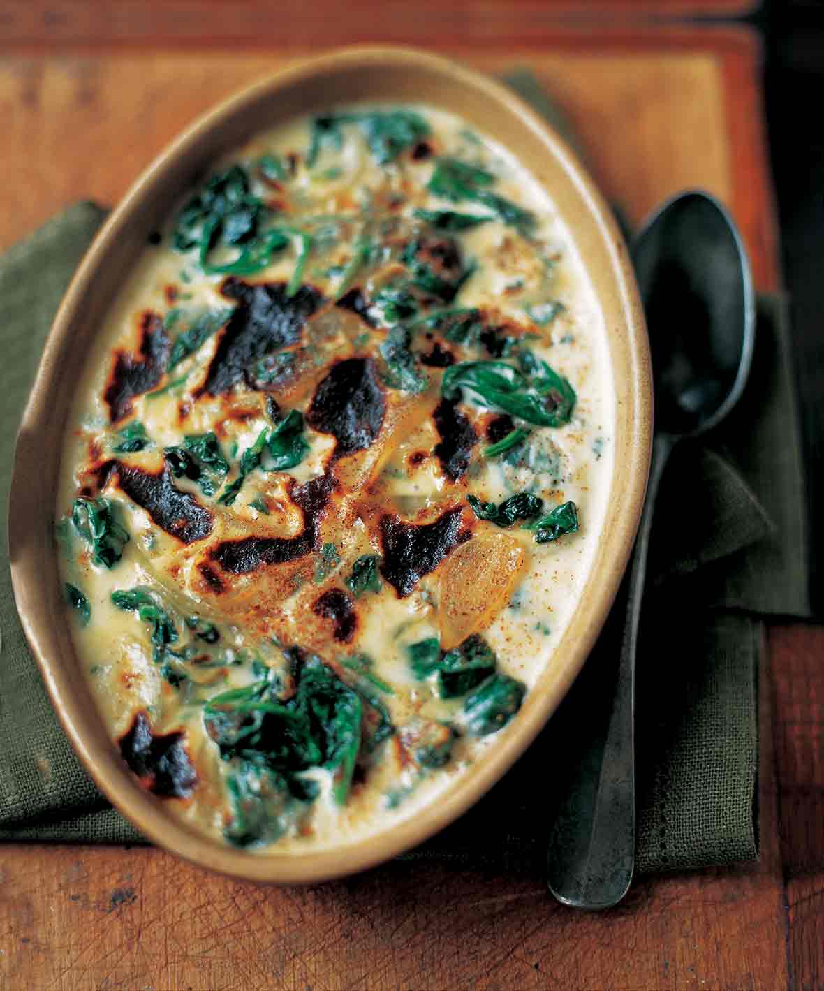 A ceramic oval dish of baked spinach mornay with cream sauce, sliced onion, and browned top.