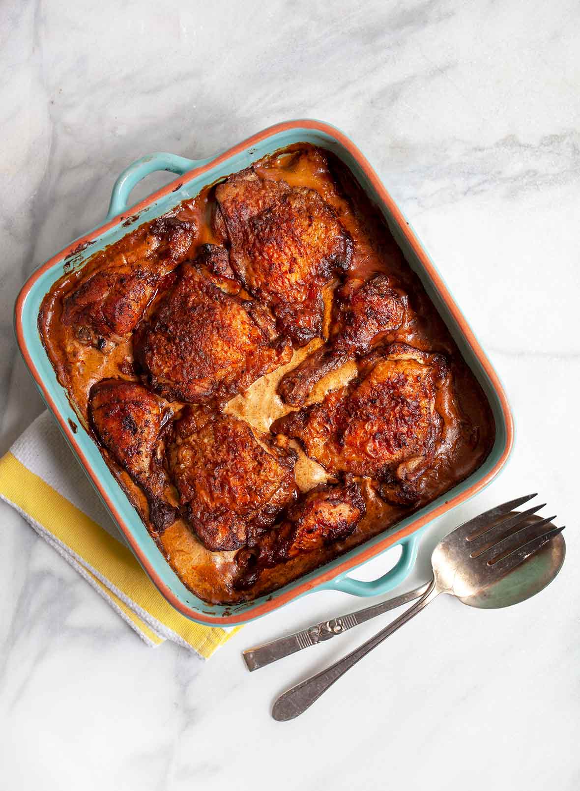 A blue earthenware dish with chicken paprikash--chicken thighs in a creamy paprika sauce, on a marble counter