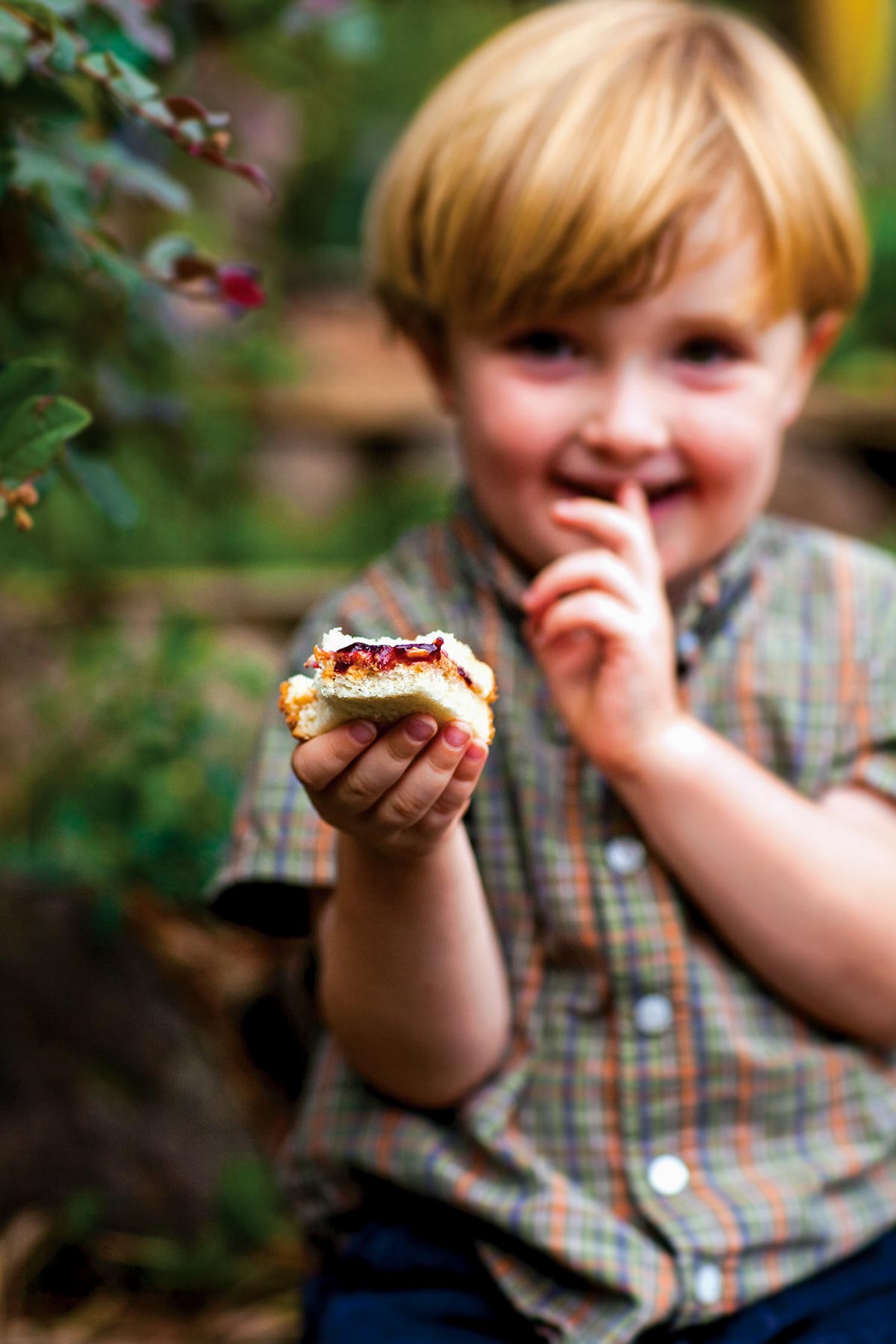 A small boy holding a partially eaten peanut butter and concord grape jam sandwich.