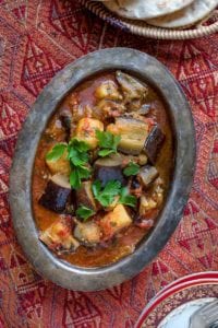 A metal serving dish of eggplant stew, called kawaj in Syria, filed with chunks of eggplants, potatoes, tomatoes with parsley on top